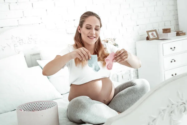 Positivo mulher grávida ativa observando meias minúsculas — Fotografia de Stock