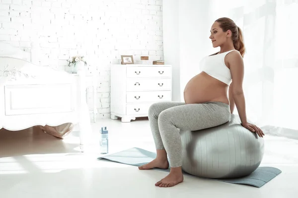 Donna dai capelli lunghi pacifici che fa esercizi mentre si siede sulla palla pilates — Foto Stock