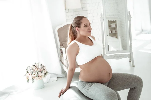 Calm good-looking woman with opened stomach sitting on rubber ball — Stock Photo, Image