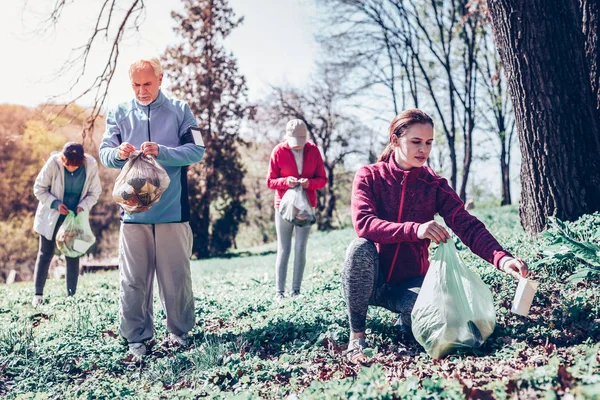 Cuatro personas socialmente activas recogiendo basura en el bosque — Foto de Stock