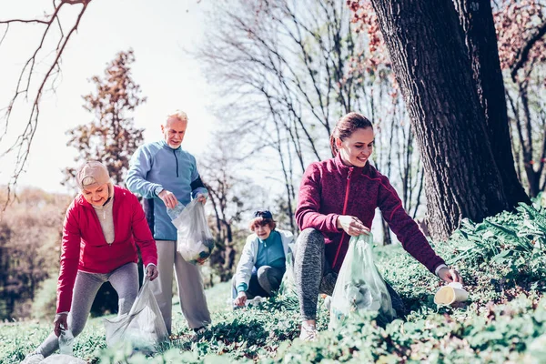 Pensionärer och unga kvinna rengöring skogen tillsammans — Stockfoto