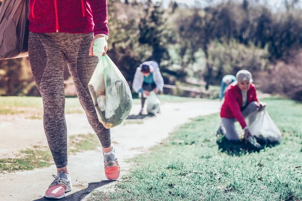 Het dragen van de beenkappen en sneakers zorg tas met vuilnis vrouw — Stockfoto