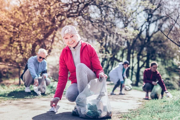 Mujer jubilada usando gorra limpiando el parque de plástico — Foto de Stock