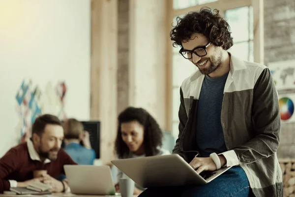 Positiv lächelnder dunkelhaariger Mann, der an einem Laptop arbeitet — Stockfoto