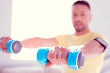 Olgun adam sabah spor yaparken mavi barbell tutan sarı gömlek giymiş