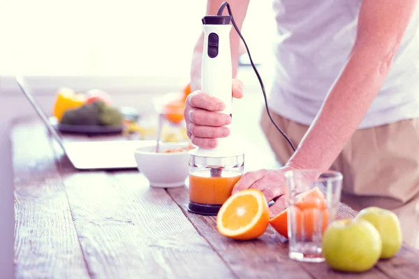 Man standing near the table while blending oranges and apples for juice — Stock Photo, Image