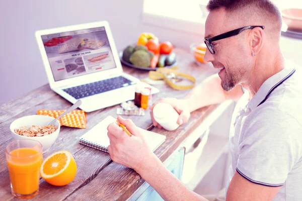 Bearded man wearing glasses feeling excited taking vitamins during breakfast — Stock Photo, Image