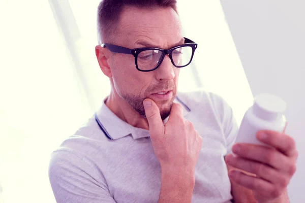 Bearded mature man with facial wrinkles feeling unsure about taking vitamins — Stock Photo, Image