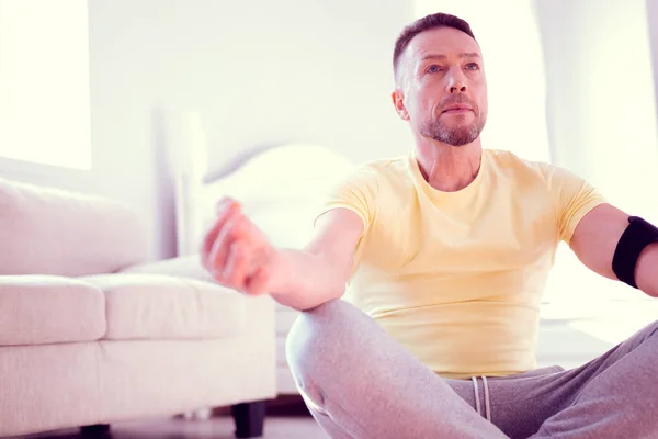 Мужчина в серых брюках и жёлтой рубашке сидит в позе лотоса медитируя — стоковое фото