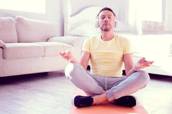 Bearded man with white earphones feeling amazing while meditating