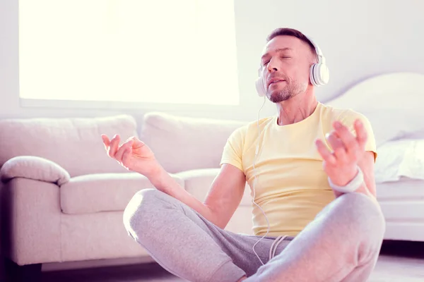 Homem vestindo camisa amarela ouvindo música relaxante e meditando em casa — Fotografia de Stock