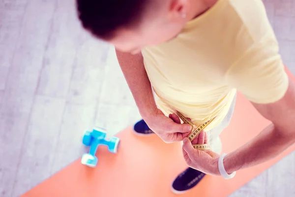 Blonde-haired man wearing blue sneakers measuring his waistline after sport time — Stock Photo, Image
