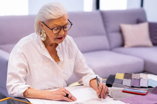 Mujer anciana sonriente en gafas haciendo boceto de diseñador — Foto de Stock