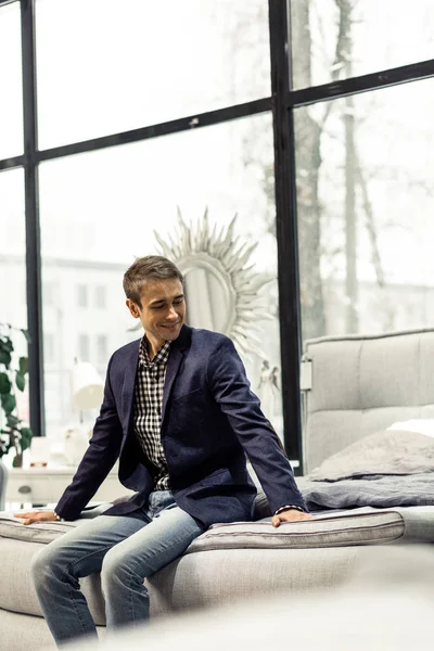 Schicker sympathischer Mann, der im Geschäft auf dem Bett sitzt — Stockfoto