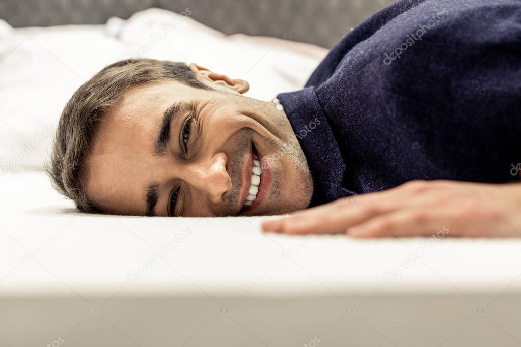 Portrait of smiling male face lying on white bed sheets