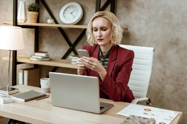 Allvarlig blond affärskvinna kontrollera hennes smartphone under lång dag — Stockfoto