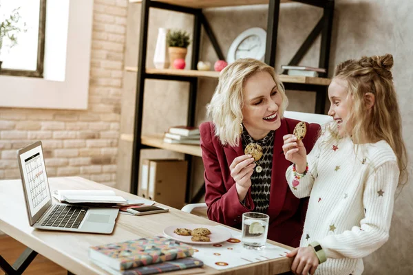 Alegre madre positiva llevando galleta y mirando a su hija riendo —  Fotos de Stock