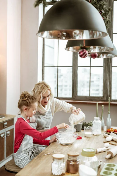 母亲和女儿穿着条纹围裙, 在木制厨房的桌子上做饭 — 图库照片