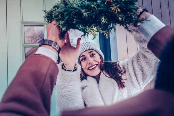Moglie indossa cappello caldo prendendo ghirlanda di Natale per decorare la casa — Foto Stock