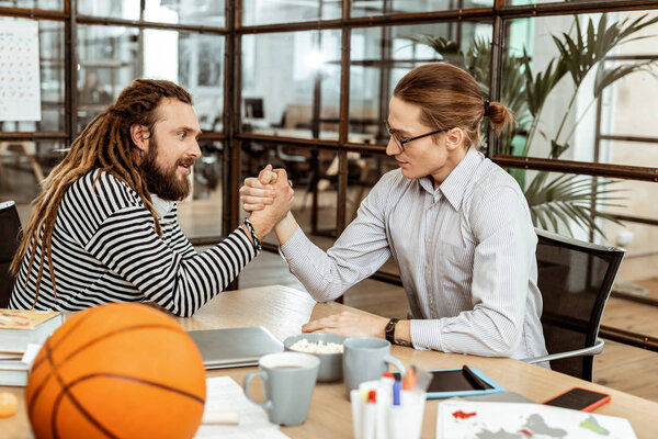 Nice young men doing armwrestling in the office