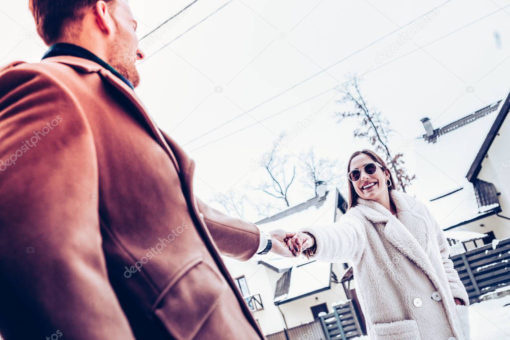 Man wearing brown coat holding hand of tender beautiful wife