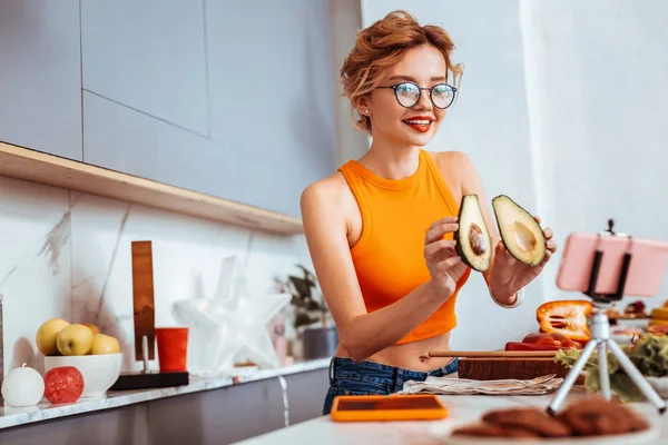 Lycklig smal kvinna visar avocado halvor till hennes publik — Stockfoto