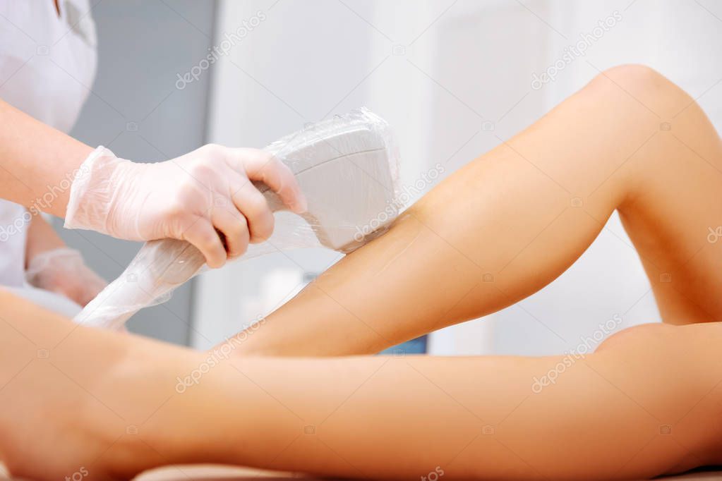 Close up of woman making laser depilation of legs for her client