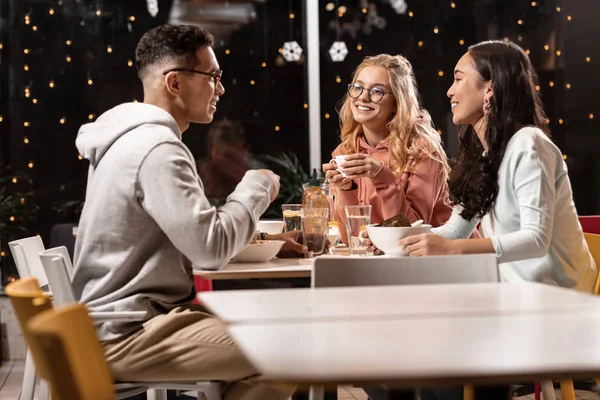 Duas garotas sentadas à mesa e ouvindo entusiasticamente o que o cara lhes diz . — Fotografia de Stock