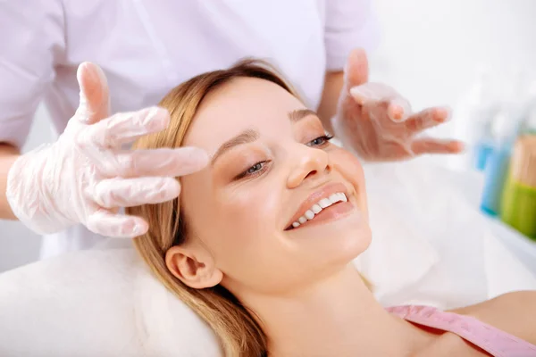 Cosmetologist making face massage of beautiful smiling client