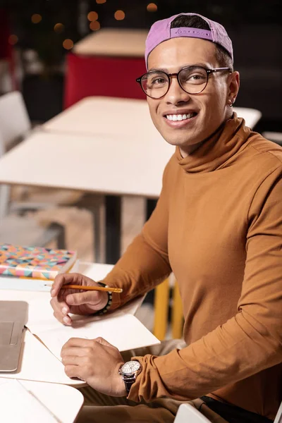 Afro-americano de boné sentado à mesa e olhando para a câmera . — Fotografia de Stock