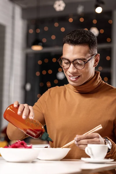 Jongeman ketchup aan het eten toe te voegen terwijl de stokjes met andere hand. — Stockfoto