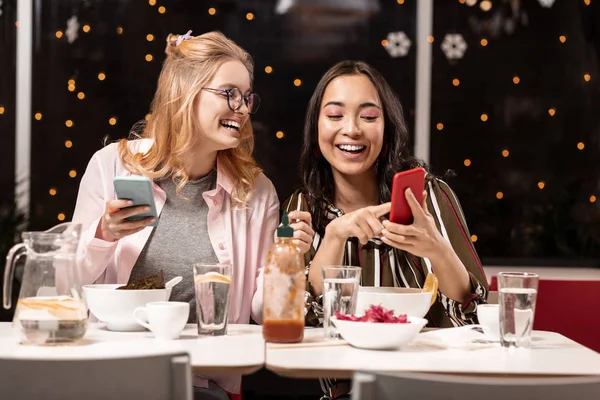 Молодые женщины смеются сидя в кафетерии и смотря видео . — стоковое фото