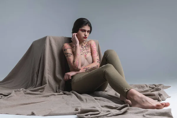 Brünette süße junge Modell mit Körperkunst in Jeans berühren ihr Ohr — Stockfoto