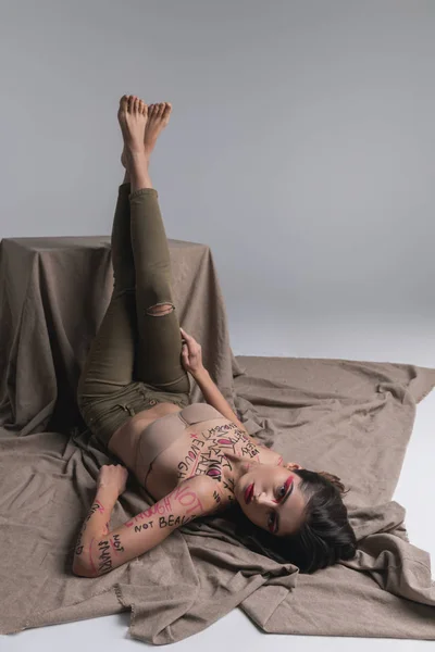 Unga brunett söt smal modell i skinny jeans höjer hennes ben upp — Stockfoto