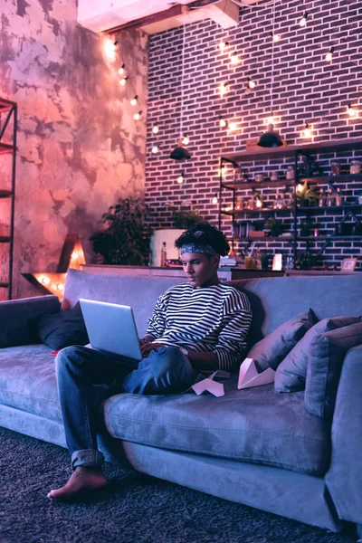 非洲裔美国人在家里工作, 坐在沙发上的电脑上. — 图库照片