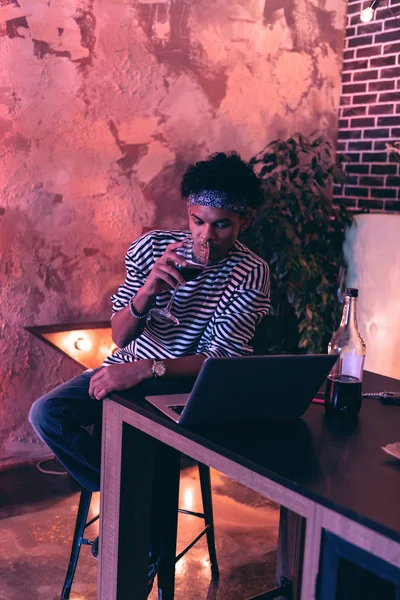 Joven bebiendo vino mientras celebra su cumpleaños con un amigo en línea . — Foto de Stock