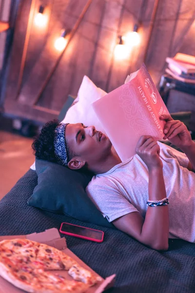 年轻的非洲裔美国人甚至晚上躺在床上看书. — 图库照片
