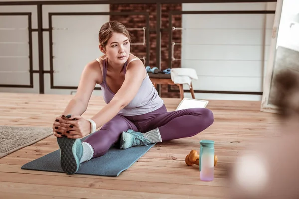 Увага жінка сидить на своєму старому килимку йоги і розігрівається — стокове фото