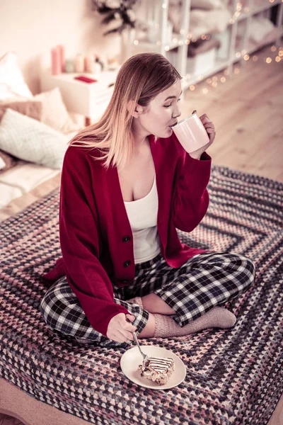 Långhåriga kvinna i röd kofta smuttar varm dryck från light cup — Stockfoto