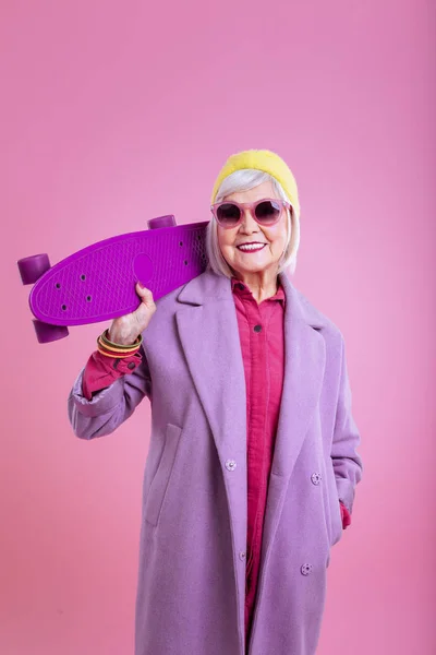 Современная сияющая пенсионерка с ярко-фиолетовым скейтбордом — стоковое фото