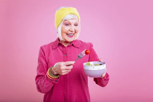 Сияющая пожилая леди в розовом платье, держащая миску с салатом — стоковое фото
