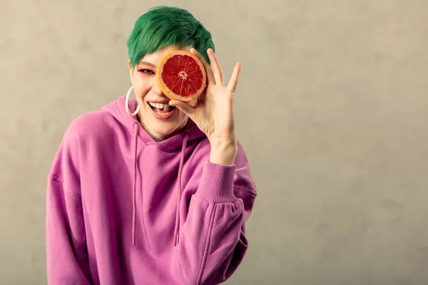 Trevlig trevlig kvinna att sätta en grapefrukt hälften till hennes öga — Stockfoto