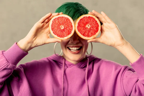 Радісна позитивна жінка прикладає половинки грейпфрута до її очей — стокове фото