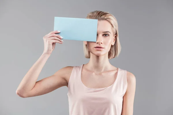 Sério mulher sem emoção fechando um olho com placa de identificação vazia — Fotografia de Stock