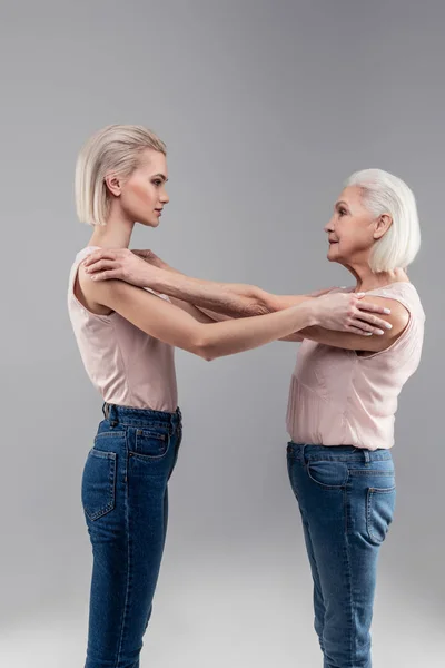 Agradable señora mayor de pelo gris abrazando a su hermosa hija rubia — Foto de Stock