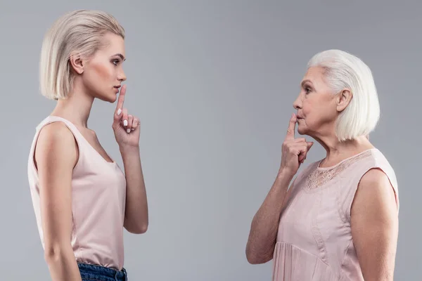 Señoras serias de pelo corto sosteniendo sus dedos cerca de la boca — Foto de Stock