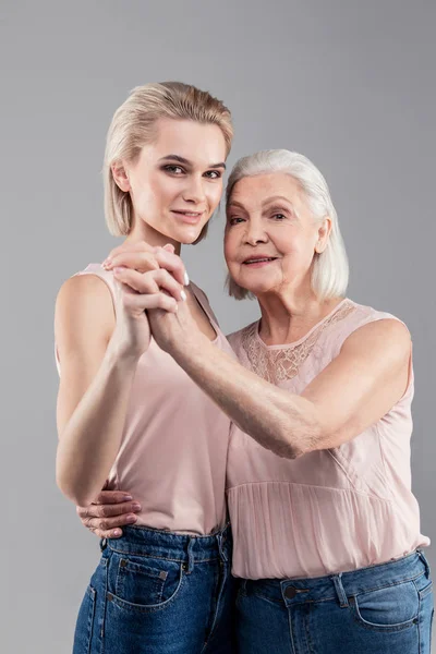 Positive tall blonde girl connecting hands and body with old woman