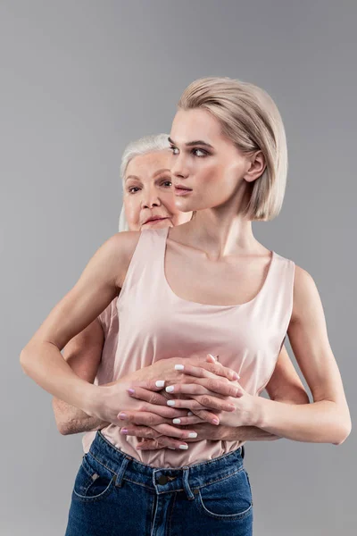 Protetora de cabelos grisalhos velha mãe abraçando sua filha jovem — Fotografia de Stock