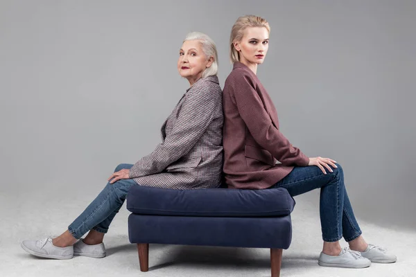 Resolute serious women sitting on blue sofa back to back — Fotografie, imagine de stoc