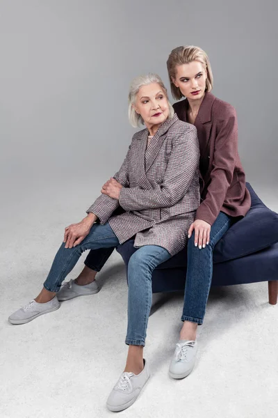 Active senior grey-haired mother sitting between legs of her beautiful daughter